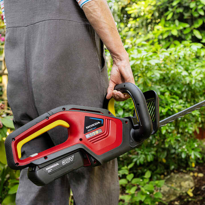Model met accu Honda heggenschaar in de tuin.
