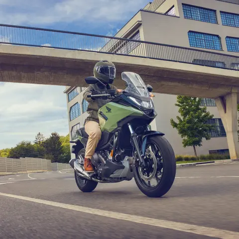 Model rijdend op de Honda NC750X motorfiets in een stedelijke omgeving.