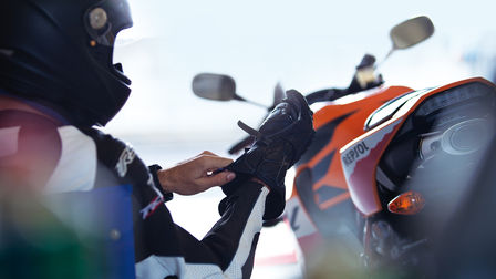 Motorrijder die zijn handschoen goed afstelt. Achterkant van motorfiets rechts van motorrijder.